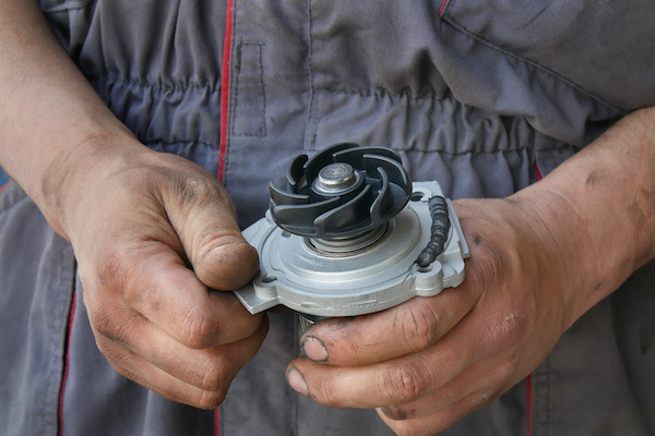 An automotive technician holding a water pump